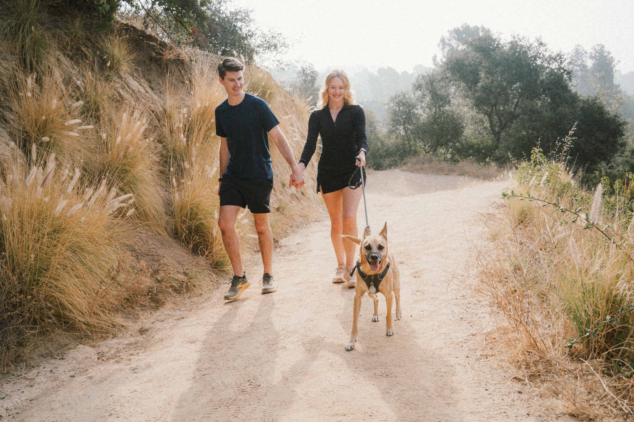 While you're here, fill in all four: Alt Text: Ollie the dog walking on a Los Angeles trail with his owners Savannah and Mitch during a documentary pet photography session